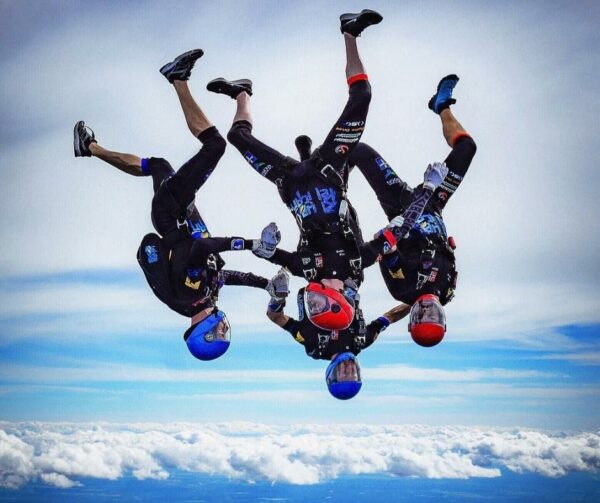 blue pelican skydiving team holding outfacing and infacing formation in freefall head down position with cloud and blue sky in background