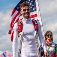 josiah rich smiling walking towards cameraman with us flag in background
