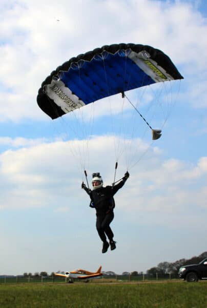 dan guest holding rear risers leaning forward in harness flying petra small plane in background photo credit andy guest