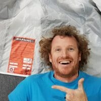 nza testie chris snelly smiling at camera lying on canopy pointing at warning label
