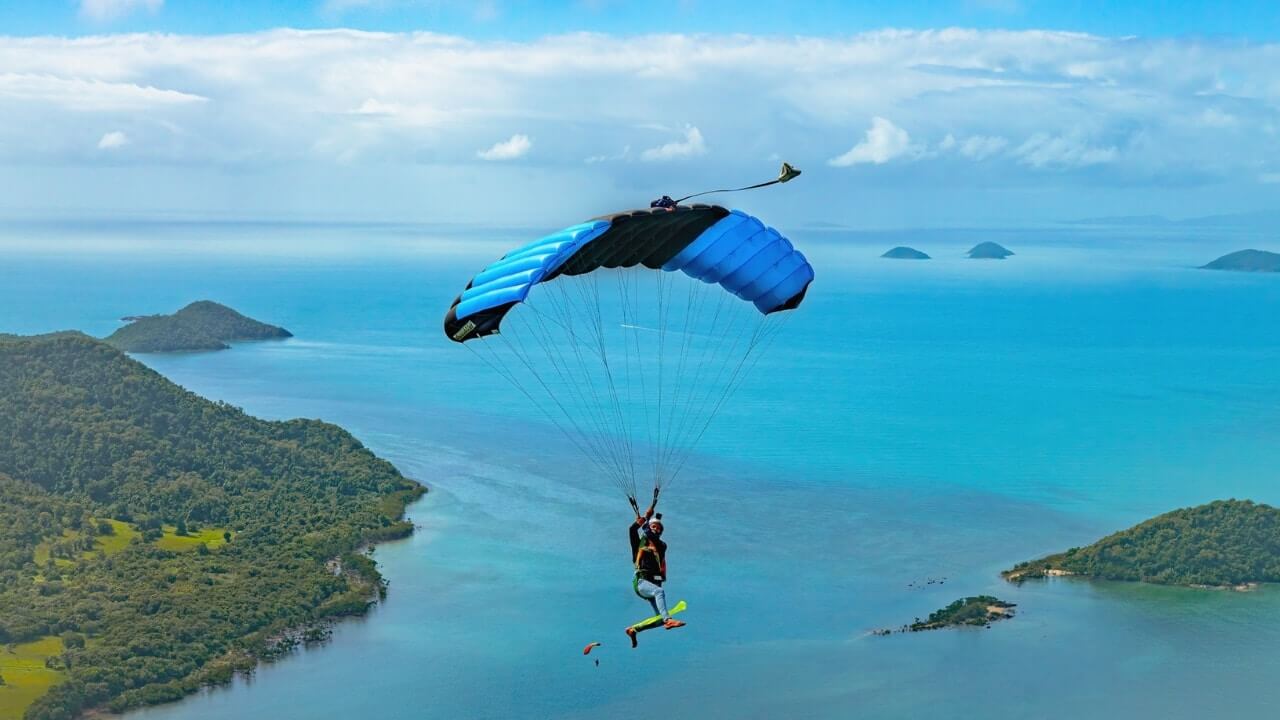 crossfire 3 skydiver under canopy looking back at camera with island and ocean background