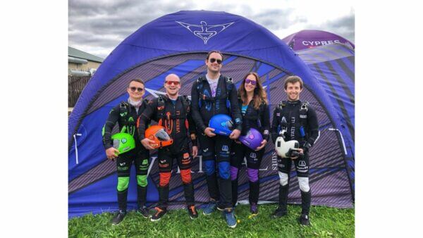 omni99 standing shoudler to shoulder holding helmets in skydive gear with tent behind them