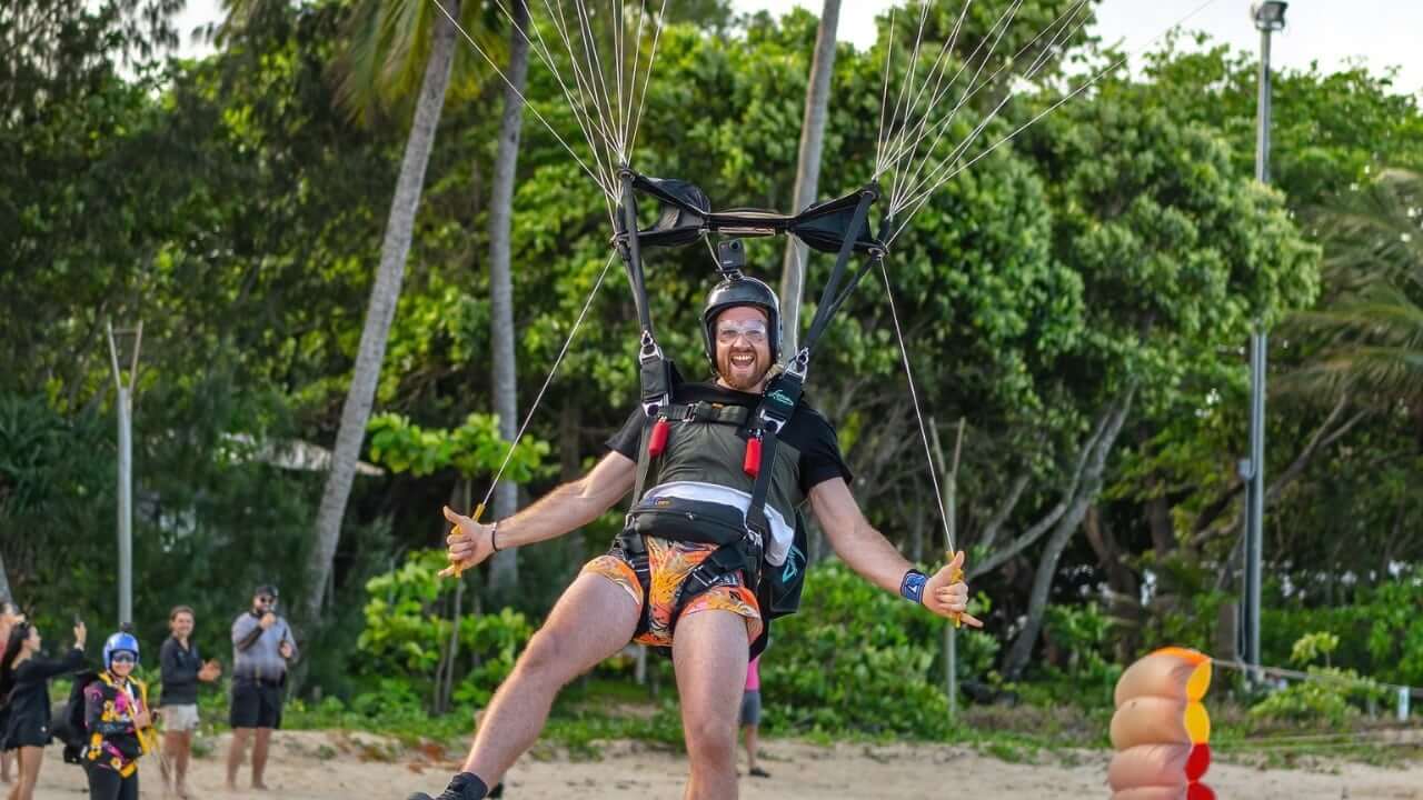 skydiver smiling at camera pulling on toggles with beach in background landing canopy